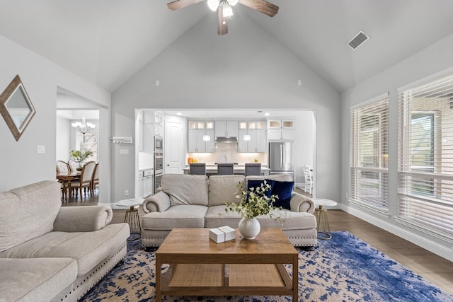 living room with dark hardwood / wood-style floors, ceiling fan with notable chandelier, and high vaulted ceiling