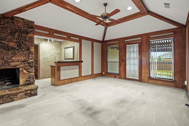 unfurnished living room with ceiling fan, light colored carpet, a stone fireplace, and beam ceiling