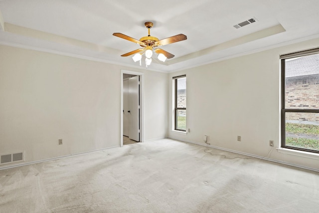 empty room with a raised ceiling, ornamental molding, light colored carpet, and ceiling fan