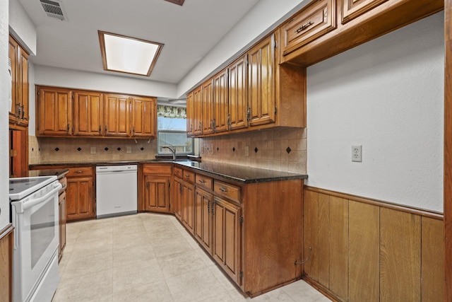 kitchen with sink, white appliances, decorative backsplash, and wood walls