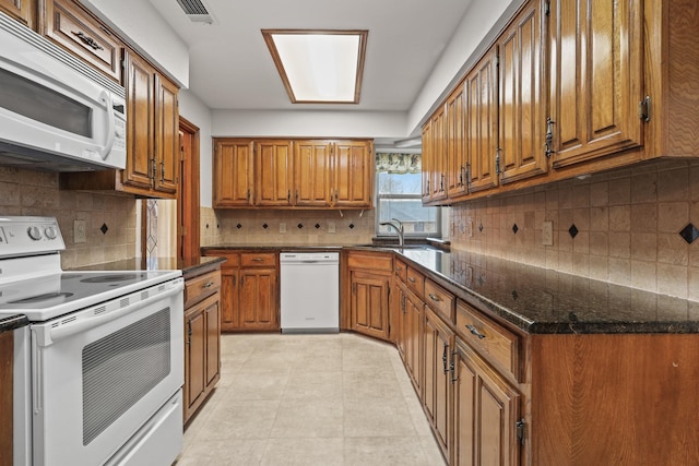 kitchen with sink, white appliances, dark stone counters, and backsplash