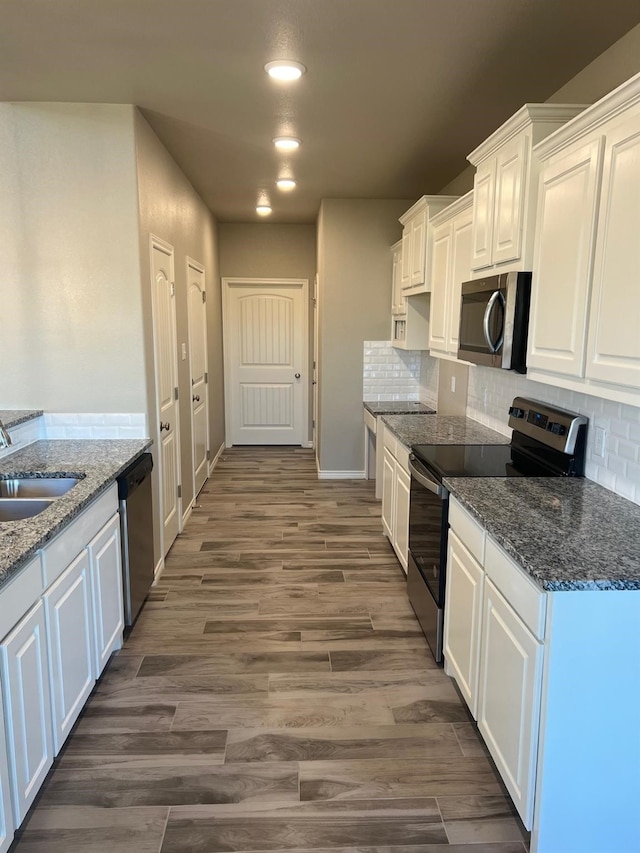 kitchen with sink, stainless steel appliances, white cabinets, dark hardwood / wood-style flooring, and dark stone counters