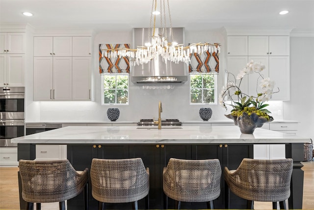 kitchen with light stone counters, white cabinets, stainless steel appliances, and a large island with sink