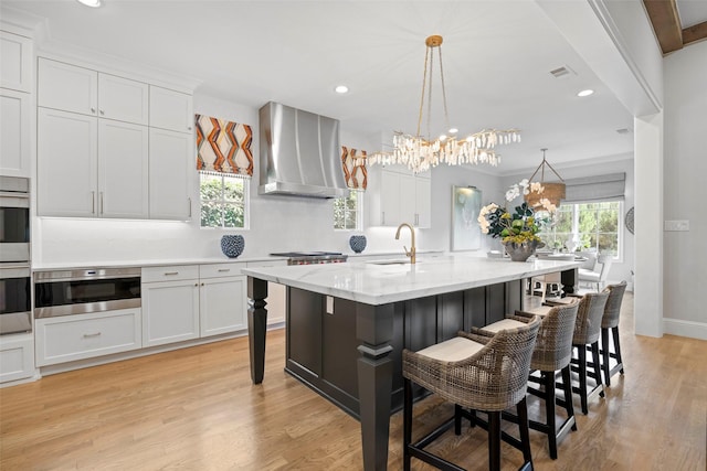 kitchen with a kitchen island with sink, wall chimney range hood, pendant lighting, and a breakfast bar