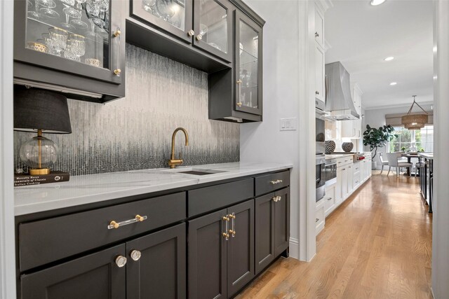 kitchen featuring extractor fan, sink, backsplash, light stone counters, and light hardwood / wood-style flooring