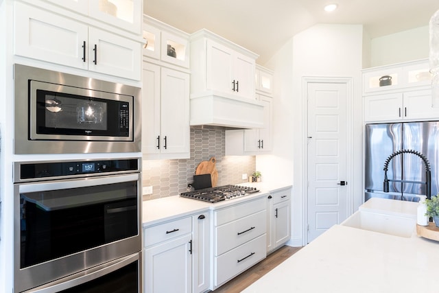 kitchen with white cabinetry, backsplash, stainless steel appliances, light hardwood / wood-style floors, and vaulted ceiling