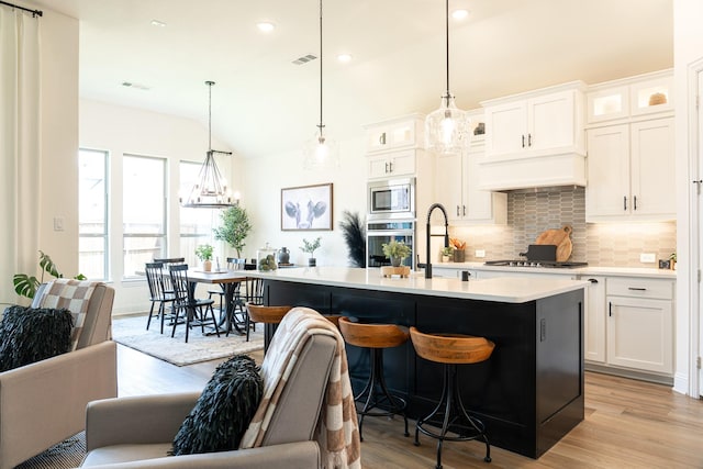 kitchen with hanging light fixtures, an island with sink, appliances with stainless steel finishes, and white cabinets