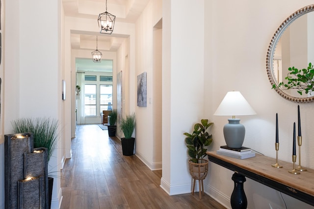 hall featuring a raised ceiling, dark wood-type flooring, and an inviting chandelier