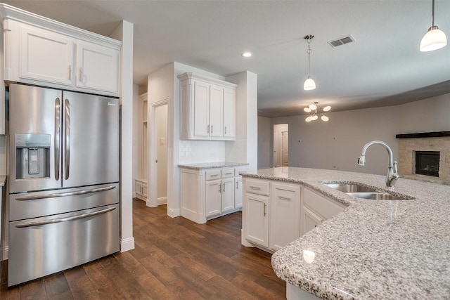 kitchen with white cabinetry, stainless steel fridge, decorative light fixtures, and sink