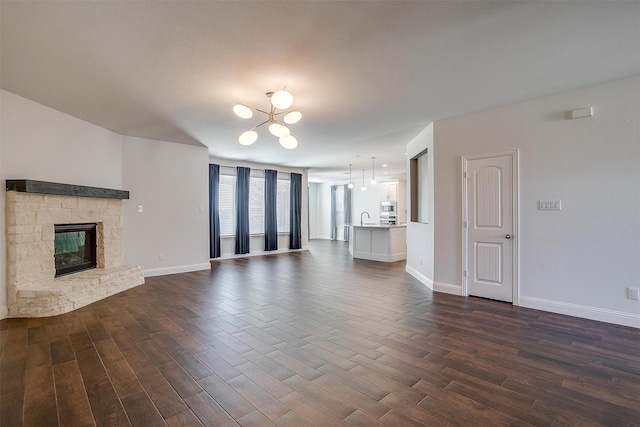 unfurnished living room featuring a stone fireplace, dark hardwood / wood-style floors, sink, and a chandelier