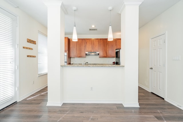 kitchen with dark wood-type flooring, light stone counters, decorative light fixtures, kitchen peninsula, and ornate columns