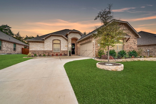 french country inspired facade with a garage, concrete driveway, brick siding, and a lawn