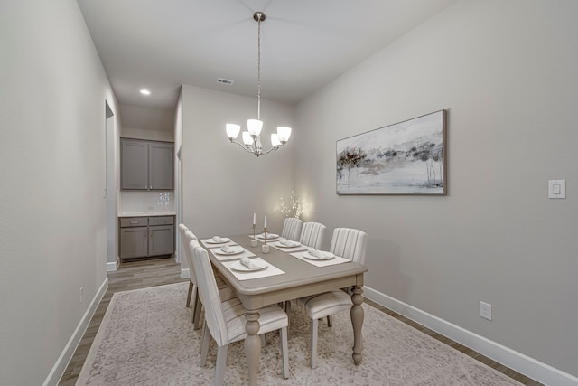 dining room featuring visible vents, light wood-style flooring, baseboards, and an inviting chandelier