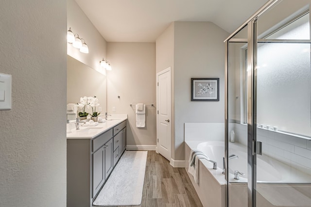 bathroom featuring a bath, double vanity, wood finished floors, and a sink