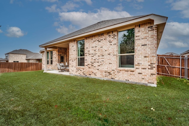 rear view of house with a patio, brick siding, a fenced backyard, and a lawn