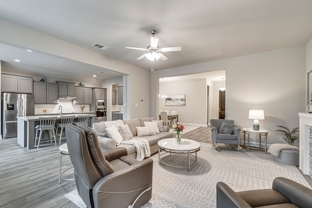 living area with visible vents, recessed lighting, ceiling fan, a glass covered fireplace, and light wood-type flooring