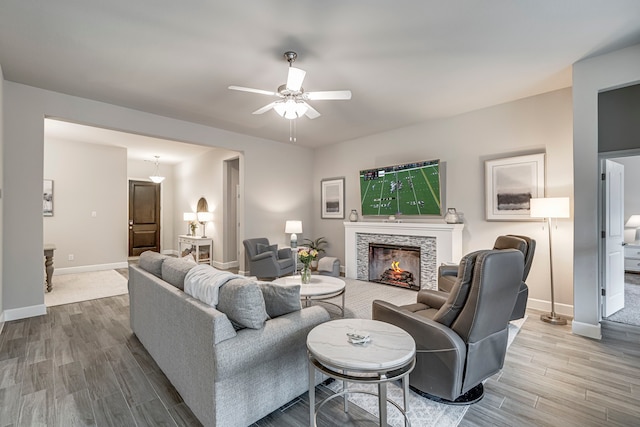 living room with ceiling fan, a fireplace, baseboards, and wood finished floors