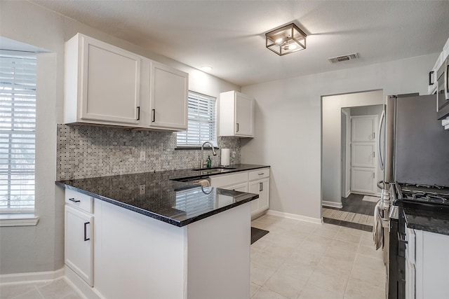 kitchen with sink, appliances with stainless steel finishes, white cabinetry, backsplash, and dark stone countertops