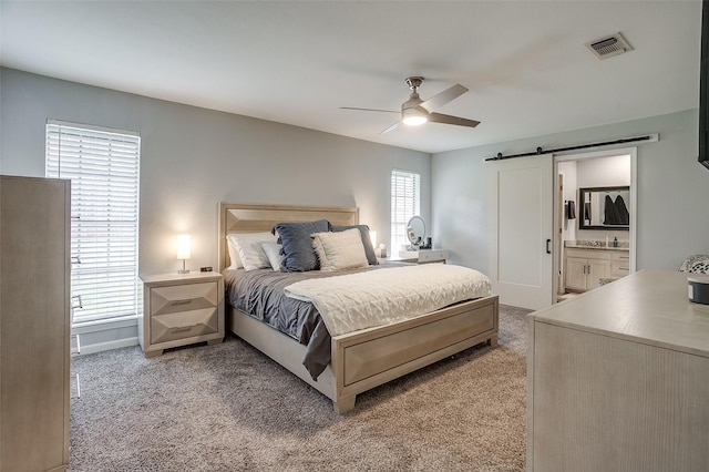 bedroom with ensuite bathroom, a barn door, light carpet, and ceiling fan