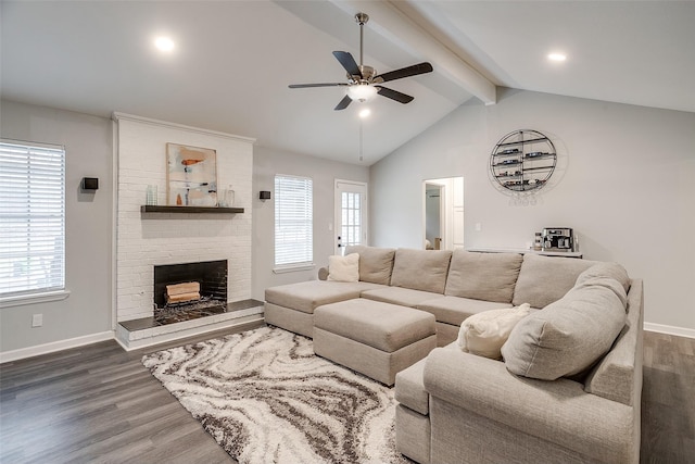 living room featuring dark wood-type flooring, a healthy amount of sunlight, a brick fireplace, and vaulted ceiling with beams