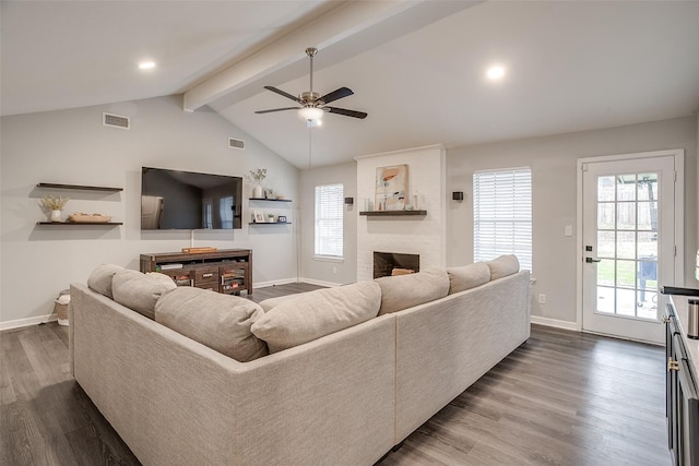 living room featuring wood-type flooring, vaulted ceiling with beams, a fireplace, and a healthy amount of sunlight