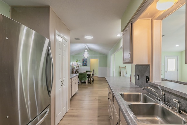 kitchen featuring sink, vaulted ceiling, light wood-type flooring, stainless steel fridge, and decorative backsplash