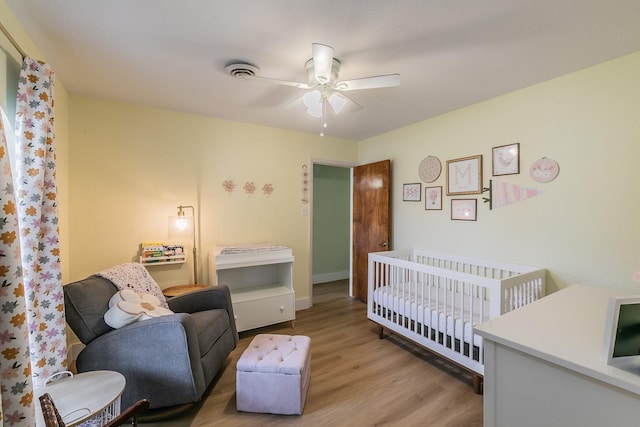 bedroom featuring a nursery area, ceiling fan, and light hardwood / wood-style flooring