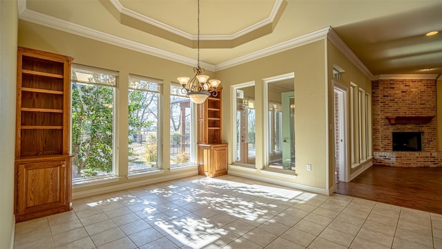 unfurnished dining area featuring light tile patterned floors, ornamental molding, a chandelier, and a brick fireplace