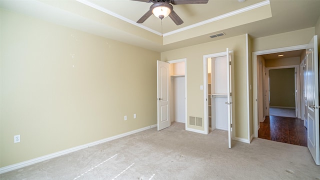 unfurnished bedroom featuring crown molding, ceiling fan, a raised ceiling, and light carpet