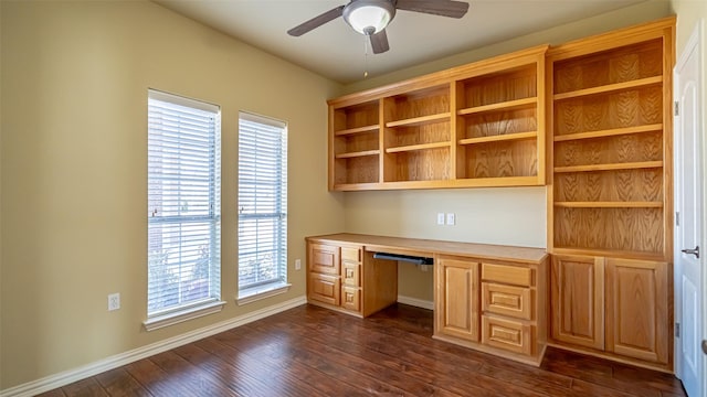 unfurnished office featuring dark hardwood / wood-style flooring, built in desk, and ceiling fan