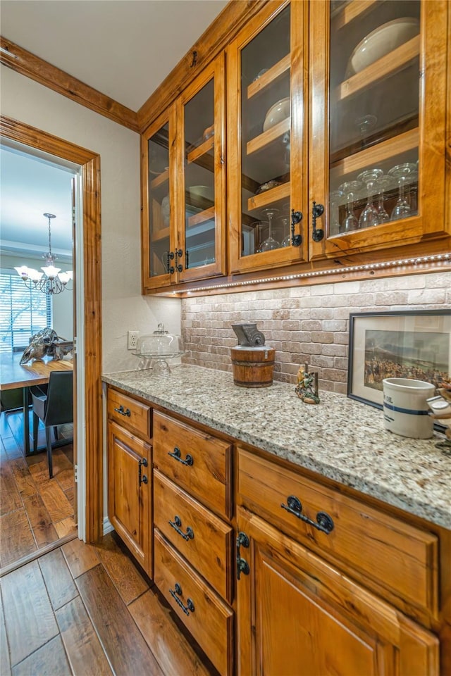 bar with dark wood-type flooring, ornamental molding, light stone countertops, and tasteful backsplash