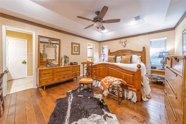 bedroom featuring wood-type flooring, ornamental molding, ceiling fan, and a tray ceiling