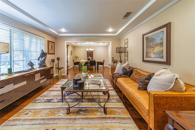 living room with ornamental molding, dark hardwood / wood-style flooring, a raised ceiling, and a notable chandelier