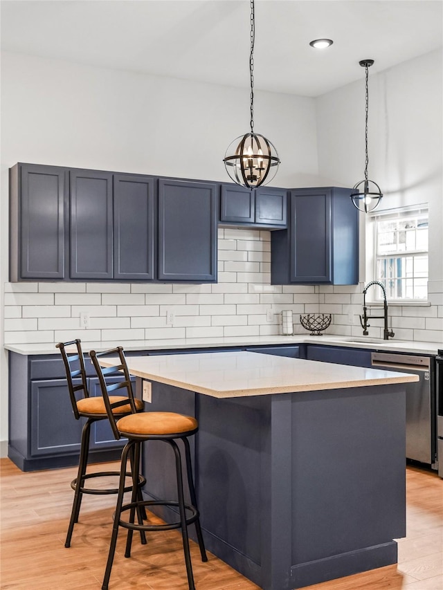 kitchen featuring blue cabinetry, hanging light fixtures, a kitchen breakfast bar, stainless steel dishwasher, and light wood-type flooring