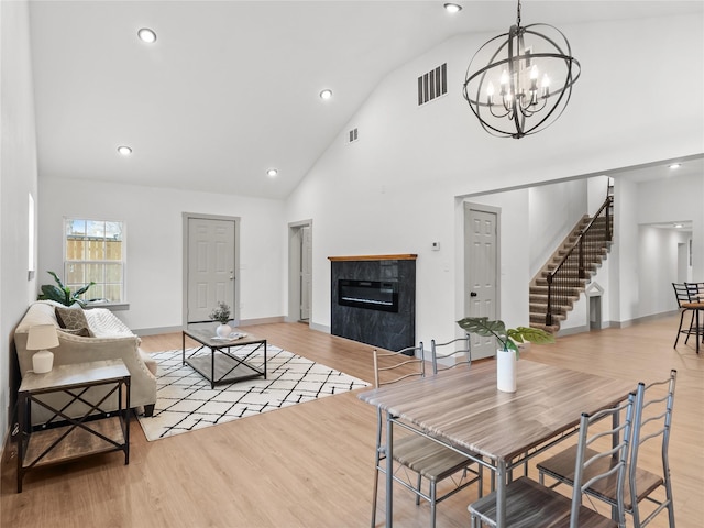 living room with a premium fireplace, high vaulted ceiling, a notable chandelier, and light hardwood / wood-style floors