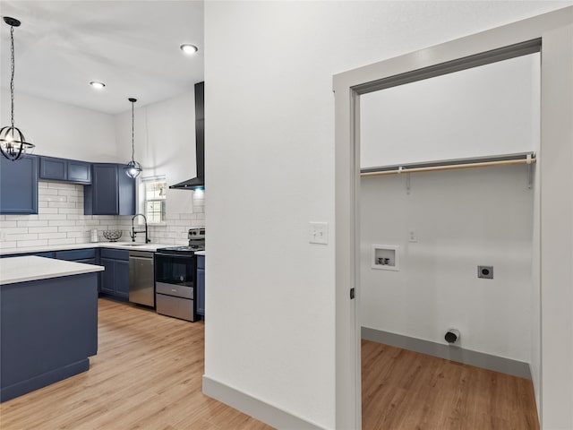 kitchen with wall chimney exhaust hood, appliances with stainless steel finishes, decorative light fixtures, and blue cabinets