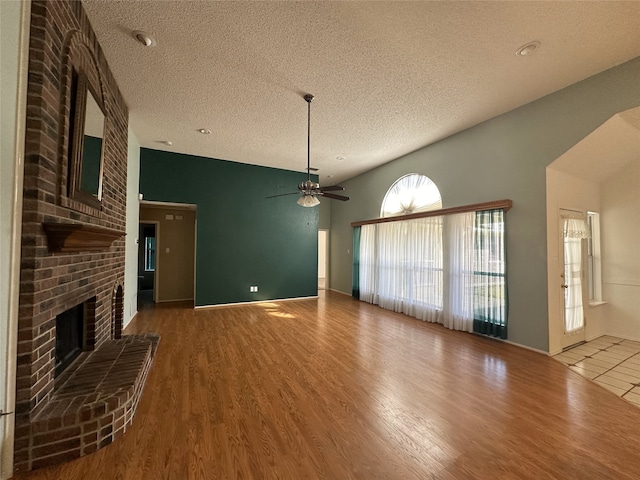 unfurnished living room with vaulted ceiling, wood-type flooring, a brick fireplace, and a textured ceiling