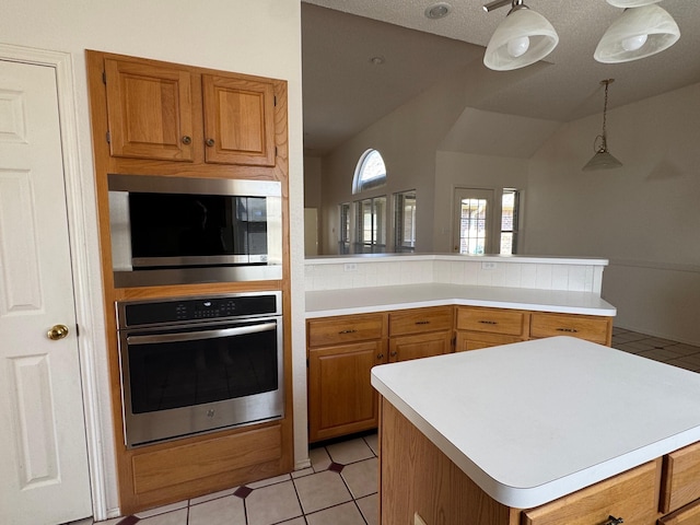 2414 W Stillwater Dr, Mesquite, TX 75181 - kitchen featuring appliances with stainless steel finishes, light countertops, a peninsula, brown cabinets, and decorative light fixtures