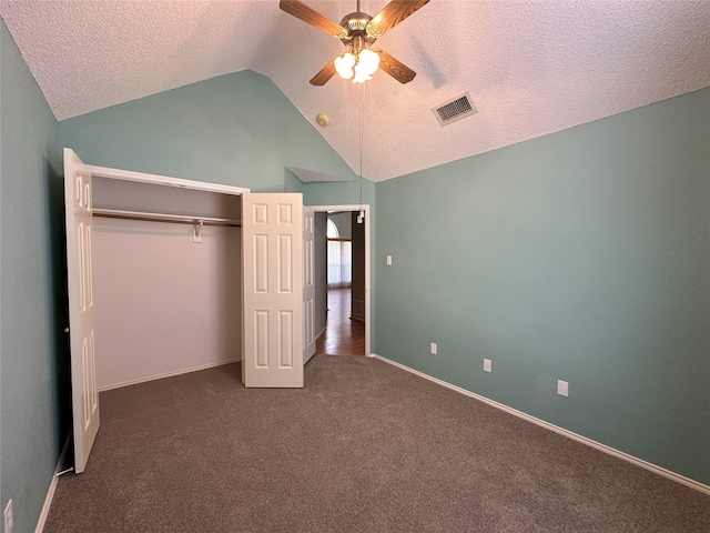 unfurnished bedroom with ceiling fan, dark colored carpet, a textured ceiling, vaulted ceiling, and a closet