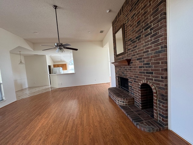 2414 W Stillwater Dr, Mesquite, TX 75181 - unfurnished living room with wood finished floors, a textured ceiling, a brick fireplace, and a ceiling fan