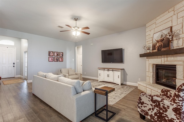 living room with dark wood-type flooring, ceiling fan, and a stone fireplace