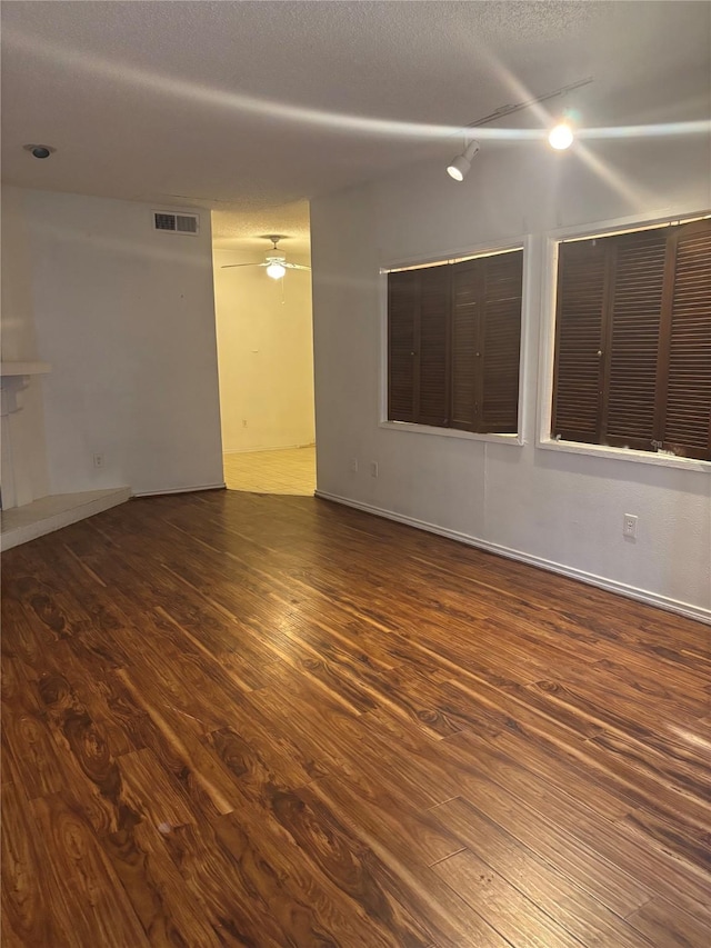 spare room featuring a tiled fireplace, dark wood-type flooring, a textured ceiling, and ceiling fan