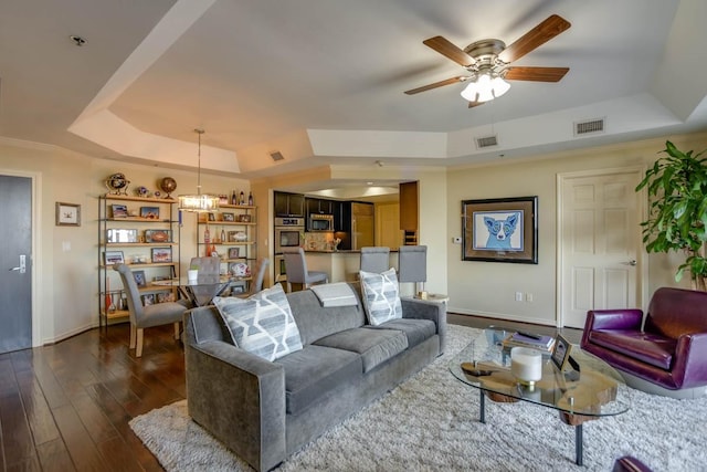 living room with dark hardwood / wood-style flooring, a raised ceiling, and ceiling fan with notable chandelier