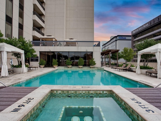 pool at dusk featuring a community hot tub, a patio area, and a gazebo