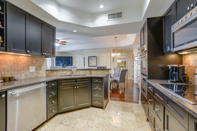 kitchen featuring pendant lighting, sink, dark stone countertops, stainless steel appliances, and a raised ceiling