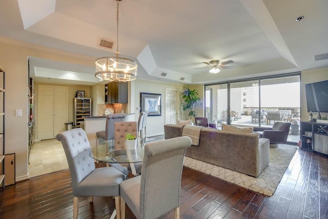 dining room with dark wood-type flooring, expansive windows, a tray ceiling, and ceiling fan with notable chandelier