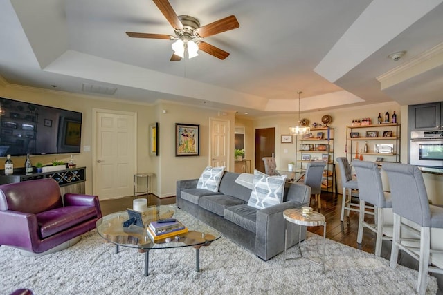 living room featuring hardwood / wood-style flooring, a tray ceiling, ceiling fan with notable chandelier, and crown molding