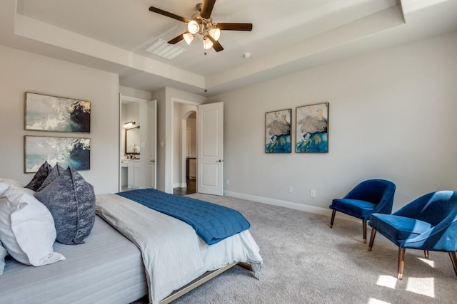 carpeted bedroom with connected bathroom and a tray ceiling