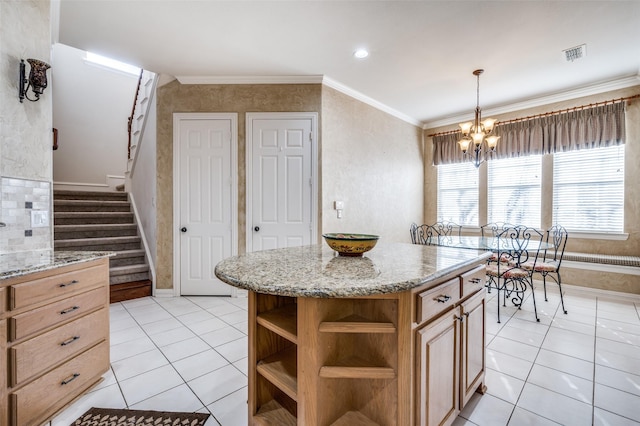 kitchen with light tile patterned flooring, crown molding, light stone counters, a center island, and a chandelier