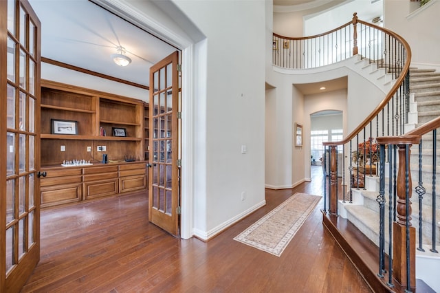 foyer entrance featuring dark wood-type flooring, ornamental molding, french doors, and a high ceiling